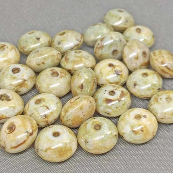 25 light golden green Picasso Czech rondelle glass beads, 9 x 6mm, scattered on a surface.